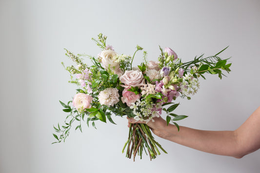 Someone holding a bouquet of light pink flowers and greenery