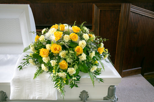 A casket spray of yellow and white roses on a white casket