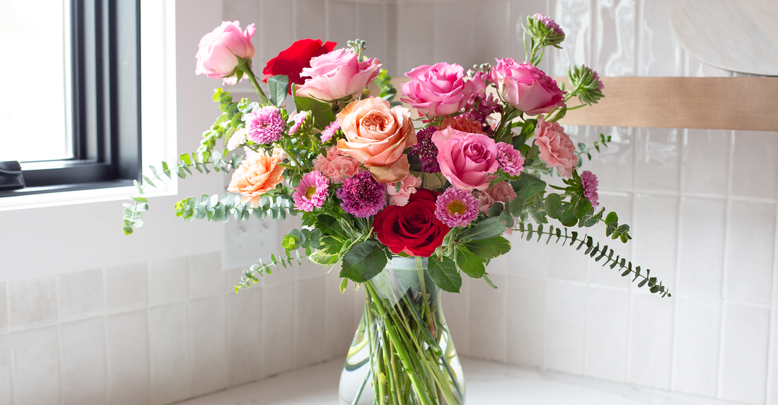 A clear vase full of pink, red, and peach roses.