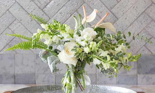 Bouquet of white flowers and greenery in a clear glass vase of water